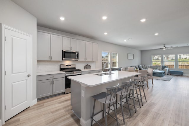 kitchen with appliances with stainless steel finishes, an island with sink, sink, a breakfast bar area, and backsplash