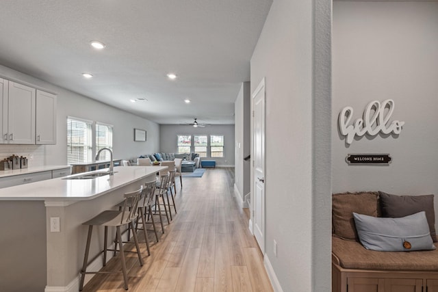 kitchen featuring white cabinets, sink, light wood-type flooring, tasteful backsplash, and a kitchen bar