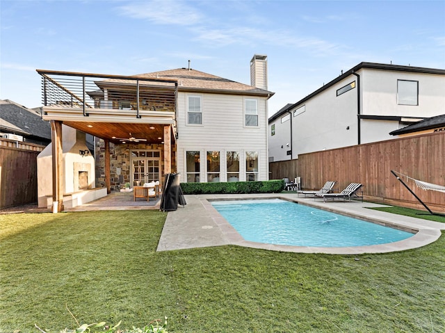 back of house with a lawn, a fenced in pool, a balcony, a fireplace, and a patio area