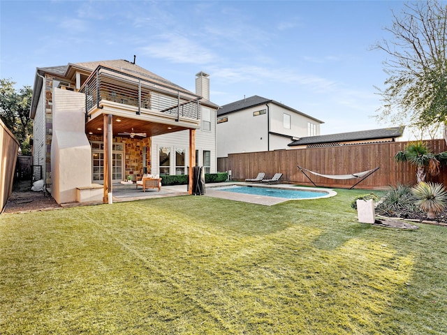 rear view of house featuring a balcony, a patio, ceiling fan, a yard, and a fenced in pool