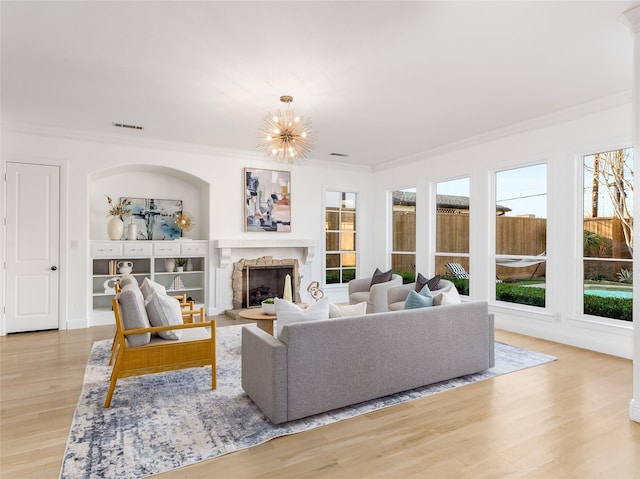 living room featuring a chandelier, light hardwood / wood-style floors, plenty of natural light, and crown molding