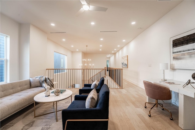 living room with ceiling fan with notable chandelier and light hardwood / wood-style flooring