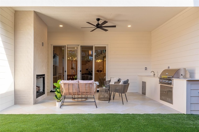 view of patio with grilling area, an outdoor living space with a fireplace, sink, ceiling fan, and exterior kitchen