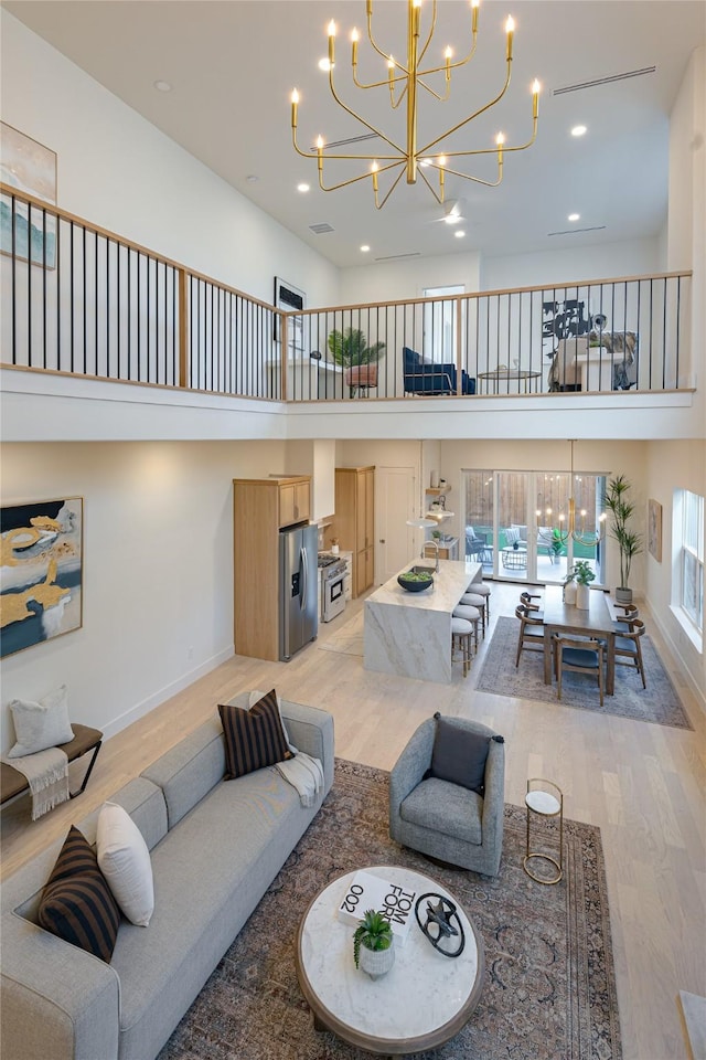 living room with a notable chandelier, light hardwood / wood-style floors, and a high ceiling