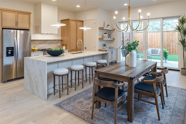 kitchen featuring pendant lighting, stainless steel fridge with ice dispenser, a kitchen island with sink, and light brown cabinetry