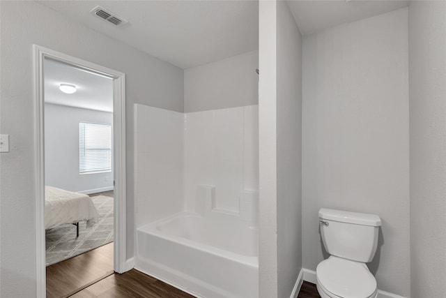 bathroom with hardwood / wood-style flooring, toilet, and shower / washtub combination