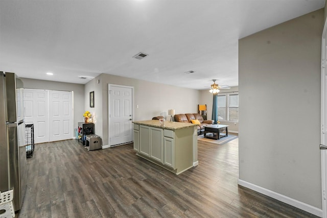 kitchen featuring ceiling fan, a center island, dark hardwood / wood-style flooring, light stone countertops, and stainless steel fridge