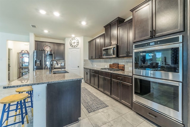 kitchen with appliances with stainless steel finishes, dark brown cabinetry, a center island with sink, and sink