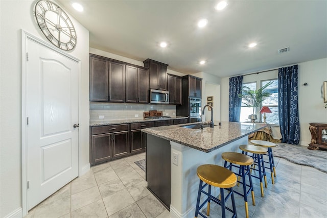 kitchen featuring a center island with sink, a kitchen breakfast bar, sink, light stone countertops, and appliances with stainless steel finishes