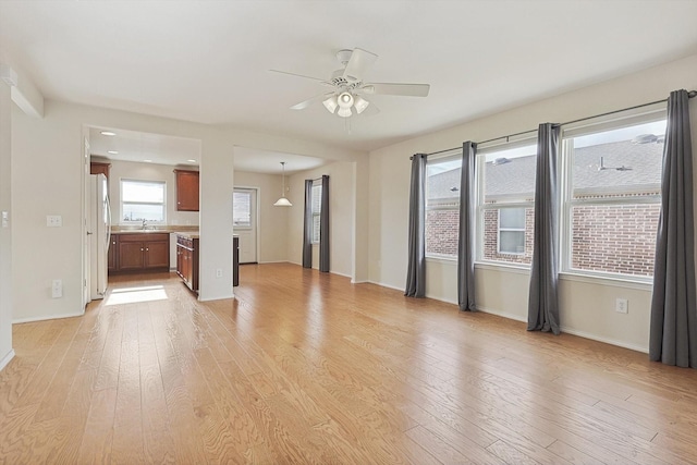 unfurnished room featuring ceiling fan, light wood-type flooring, sink, and a wealth of natural light