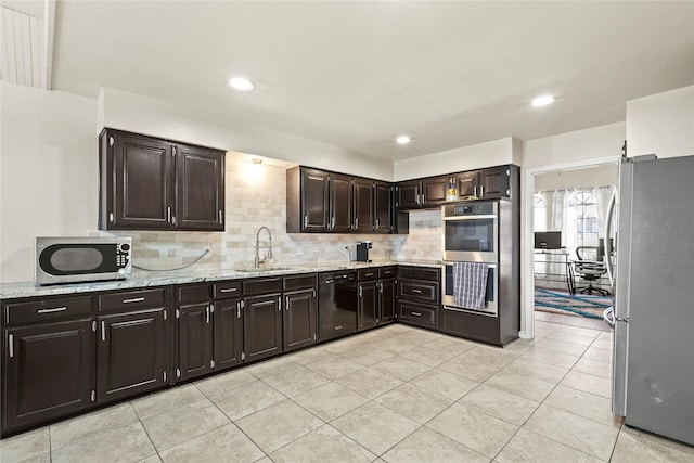 kitchen featuring sink, decorative backsplash, light stone counters, dark brown cabinetry, and stainless steel appliances