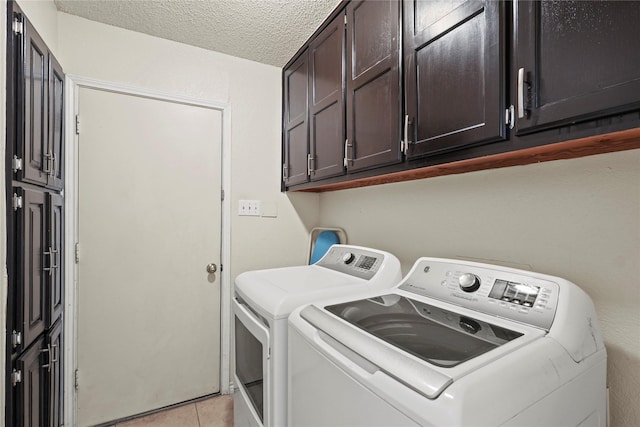 clothes washing area with washing machine and clothes dryer, light tile patterned floors, cabinets, and a textured ceiling