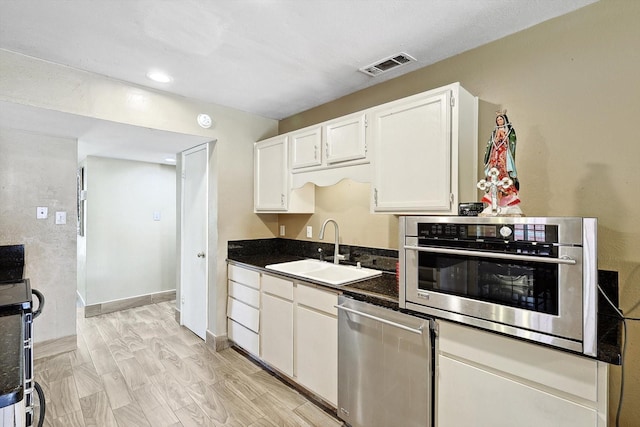 kitchen with dark stone counters, stainless steel appliances, sink, light hardwood / wood-style flooring, and white cabinets