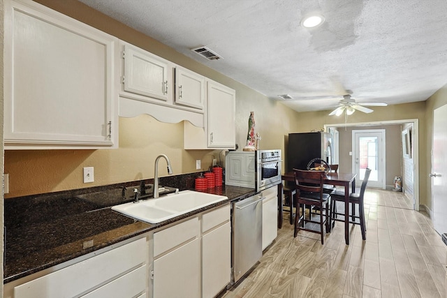 kitchen featuring stainless steel appliances, white cabinetry, dark stone counters, and sink