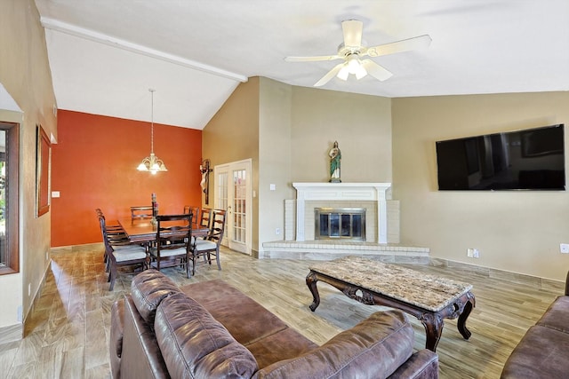 living room with lofted ceiling with beams, a fireplace, light hardwood / wood-style floors, and ceiling fan with notable chandelier