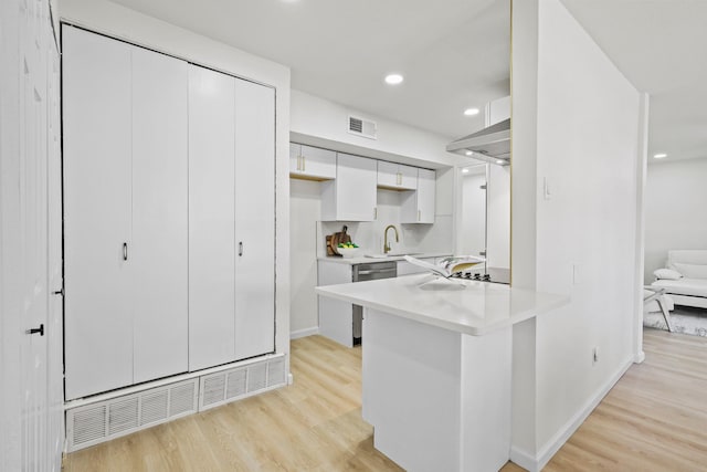 kitchen with kitchen peninsula, stainless steel dishwasher, sink, light hardwood / wood-style floors, and white cabinetry