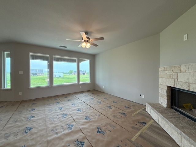 unfurnished living room featuring ceiling fan and a stone fireplace