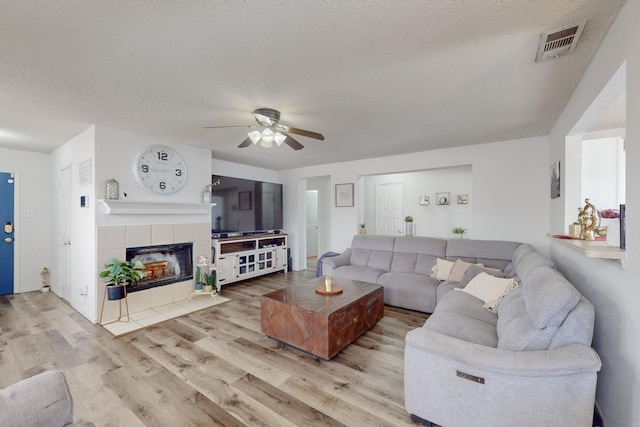 living room featuring ceiling fan, light hardwood / wood-style floors, a textured ceiling, and a tile fireplace