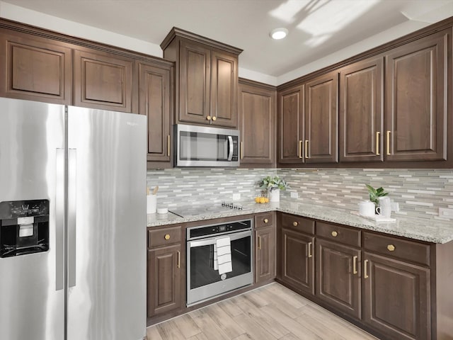 kitchen featuring appliances with stainless steel finishes, tasteful backsplash, light wood-type flooring, light stone counters, and dark brown cabinetry