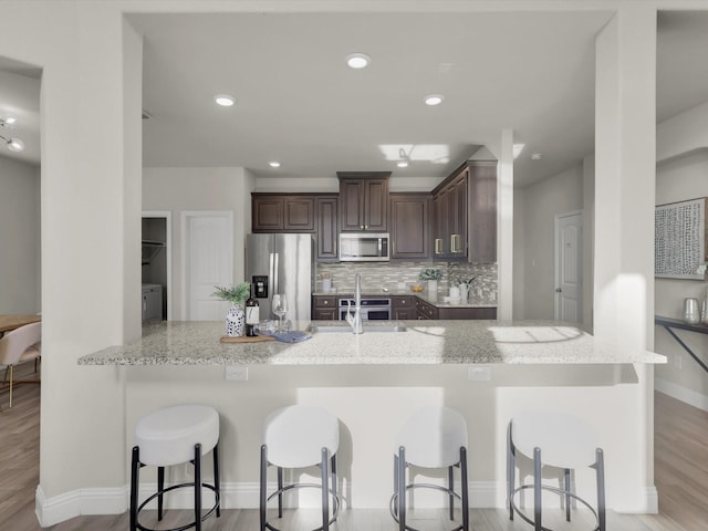 kitchen with kitchen peninsula, appliances with stainless steel finishes, decorative backsplash, light stone counters, and a breakfast bar