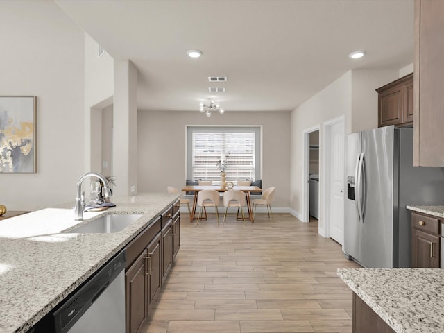 kitchen with light stone counters, sink, dark brown cabinetry, and stainless steel appliances