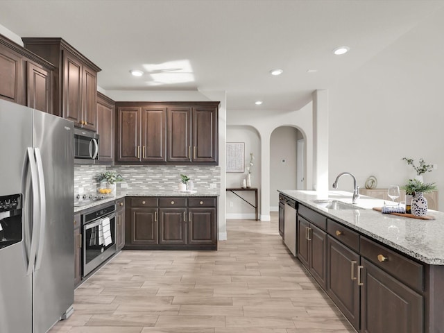 kitchen featuring dark brown cabinetry, appliances with stainless steel finishes, sink, backsplash, and light stone counters