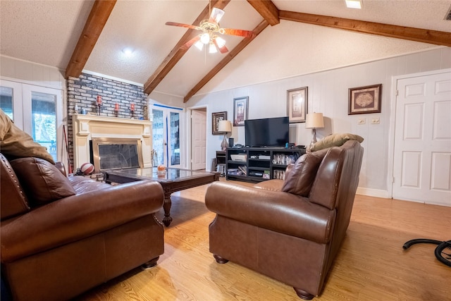 living room featuring light wood-type flooring, a textured ceiling, ceiling fan, a fireplace, and vaulted ceiling with beams