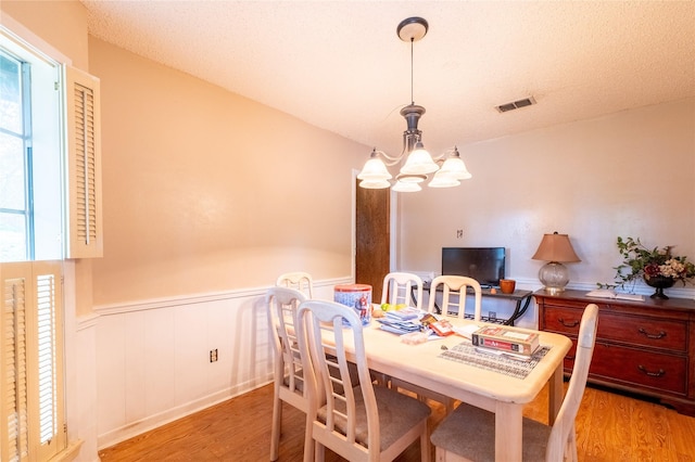 dining space with a wealth of natural light, an inviting chandelier, a textured ceiling, and light wood-type flooring