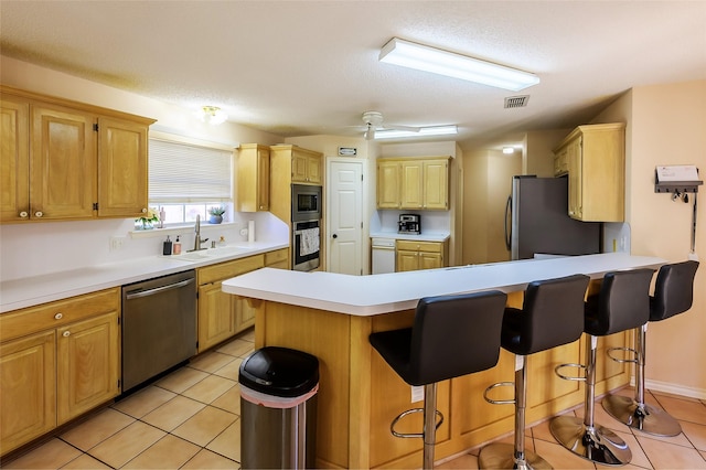 kitchen with ceiling fan, sink, stainless steel appliances, a breakfast bar, and light tile patterned floors