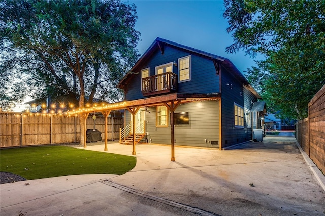 back house at dusk featuring a balcony, a patio area, and a lawn