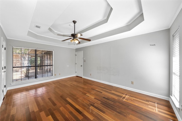 empty room with a tray ceiling, ceiling fan, crown molding, and hardwood / wood-style flooring