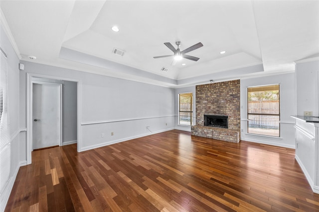 unfurnished living room featuring ornamental molding, a tray ceiling, ceiling fan, a fireplace, and dark hardwood / wood-style floors