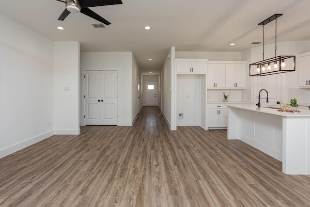 kitchen with decorative light fixtures, white cabinetry, a kitchen island with sink, and light hardwood / wood-style flooring