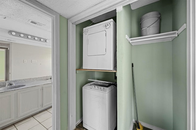 washroom featuring light tile patterned floors, a textured ceiling, stacked washer and dryer, and sink