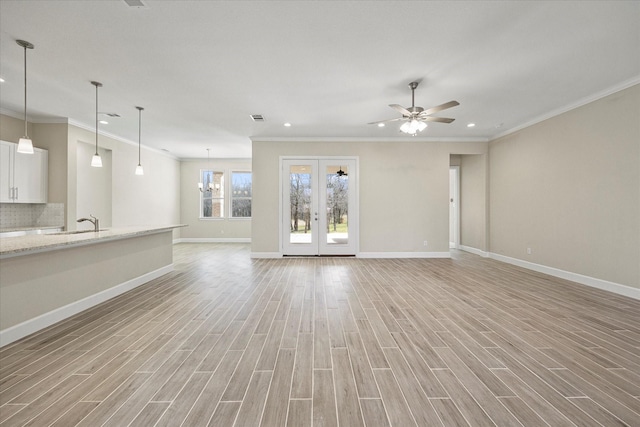 unfurnished living room with crown molding, ceiling fan with notable chandelier, light hardwood / wood-style flooring, and sink