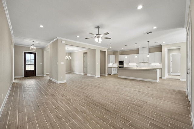 unfurnished living room with ceiling fan with notable chandelier, light hardwood / wood-style floors, sink, and ornamental molding