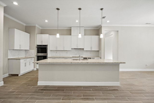 kitchen with a kitchen island with sink, light stone countertops, and white cabinetry