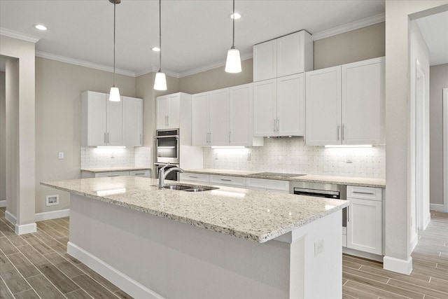 kitchen featuring an island with sink, white cabinets, light stone counters, and sink