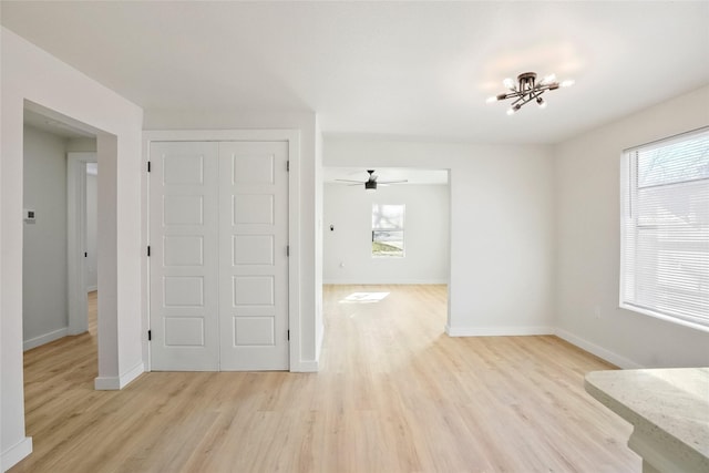 empty room featuring light hardwood / wood-style flooring, a wealth of natural light, and ceiling fan with notable chandelier