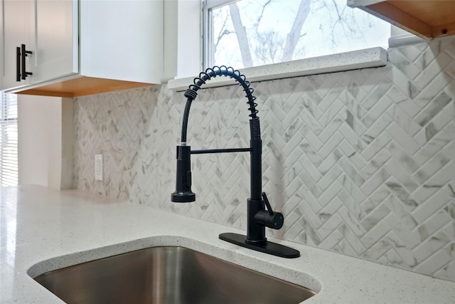 room details featuring light stone counters, white cabinets, tasteful backsplash, and sink