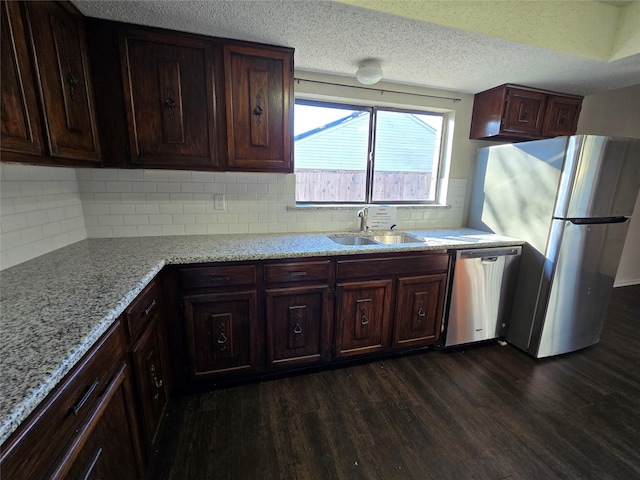 kitchen with stainless steel appliances, light stone countertops, dark hardwood / wood-style floors, sink, and dark brown cabinets