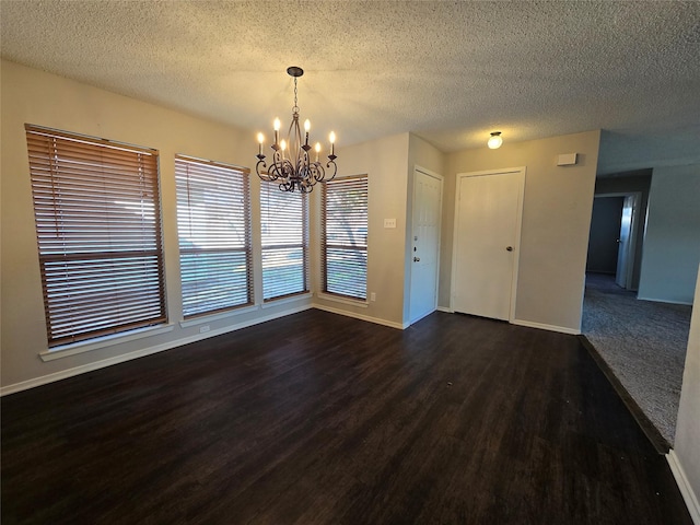 unfurnished dining area with dark wood-type flooring, a textured ceiling, and a notable chandelier