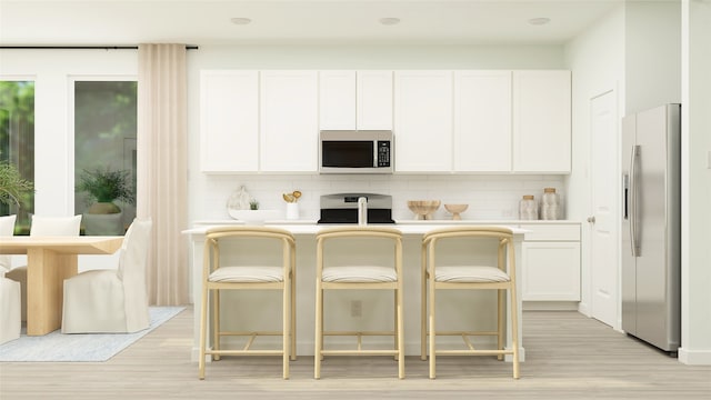 kitchen featuring decorative backsplash, stainless steel appliances, light hardwood / wood-style flooring, white cabinets, and a breakfast bar area