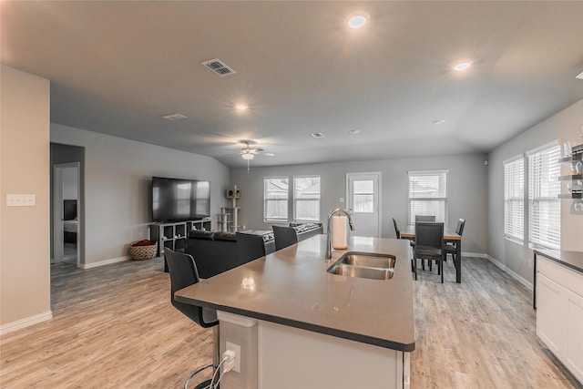 kitchen featuring light wood-type flooring, white cabinetry, sink, and an island with sink