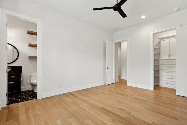 unfurnished bedroom with ensuite bath, a spacious closet, a closet, light hardwood / wood-style floors, and ceiling fan