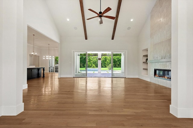 unfurnished living room featuring built in features, hardwood / wood-style flooring, high vaulted ceiling, ceiling fan with notable chandelier, and a tiled fireplace