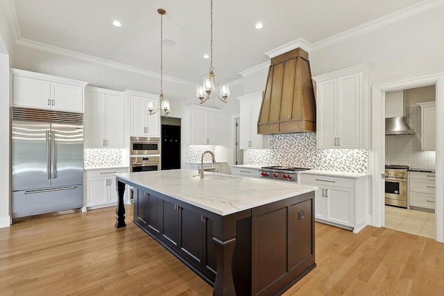 kitchen with white cabinets, high end appliances, and a center island with sink