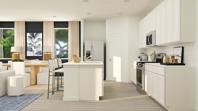 kitchen with a kitchen breakfast bar, appliances with stainless steel finishes, a kitchen island with sink, white cabinets, and light wood-type flooring