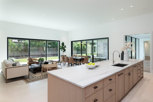 kitchen with light brown cabinetry, a kitchen island with sink, sink, and light stone counters