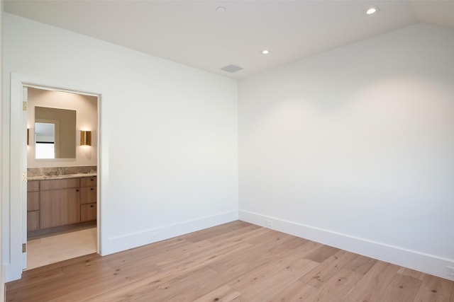 empty room with sink, light hardwood / wood-style floors, and vaulted ceiling